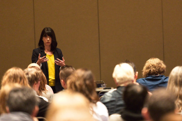 presenter at a conference gestures in front of a crowd.