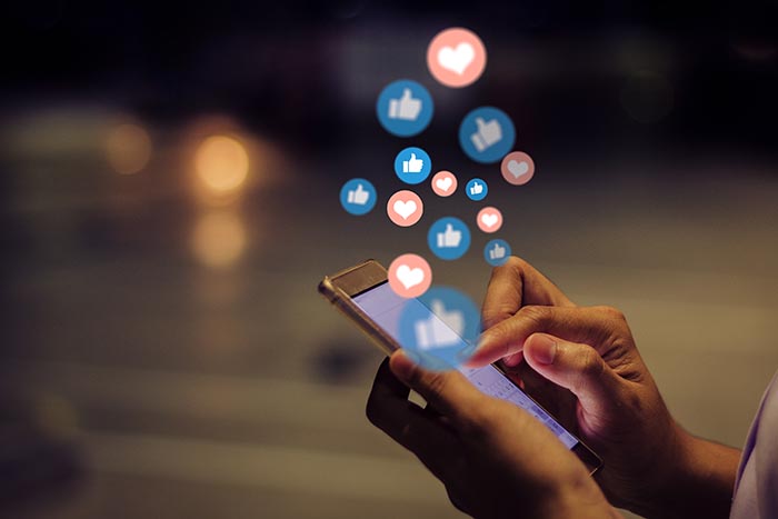 Stock photo of a person's hands holding a phone, with illustrated "like" and "heart" symbols floating up above the device.