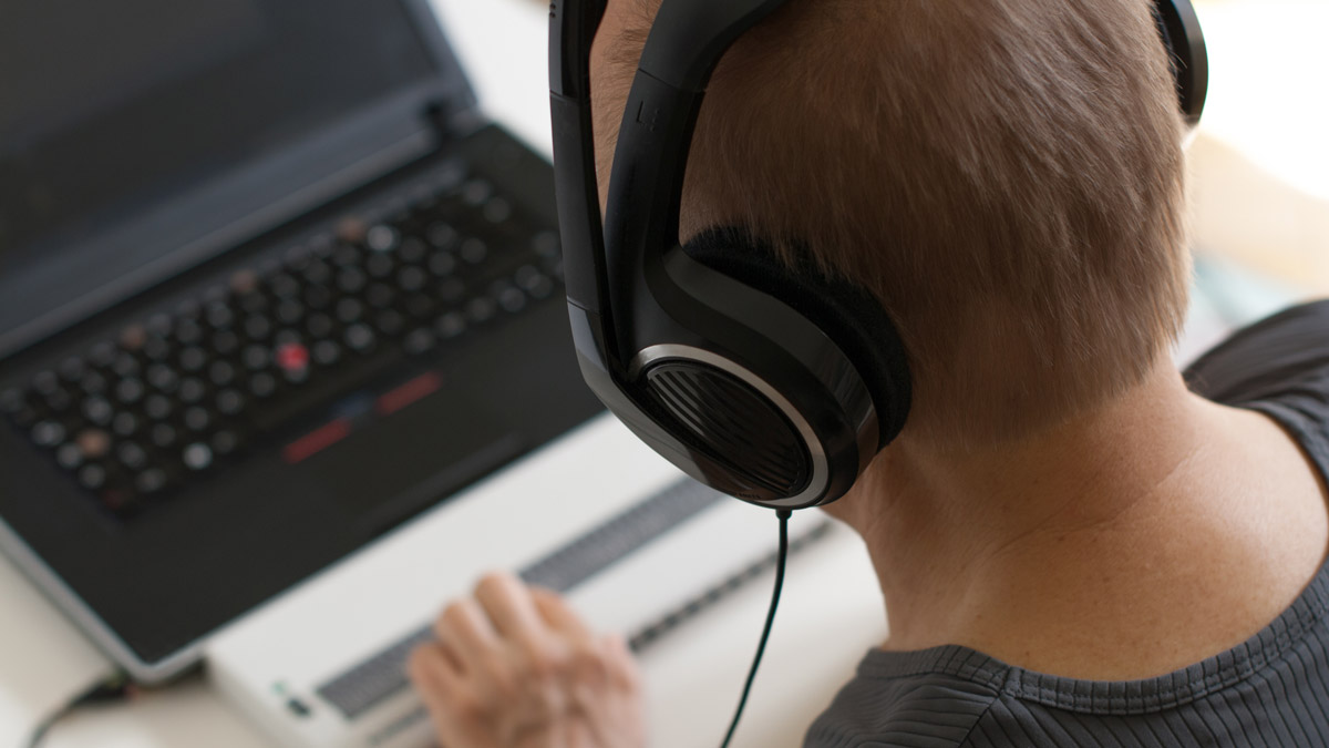 A person works on a laptop while wearing headphones