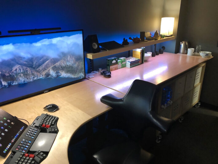 view of Jonathan's desk on the right side, with a shelf with office supplies and various knick knacks, soft lighting